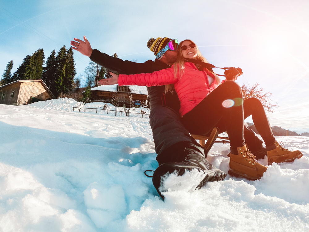 Happy couple having fun om a wood vintage sled riding down a snowy mountain.