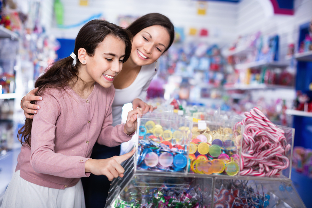 Happy positive smiling woman with emotional daughter choosing candies in the candy shop