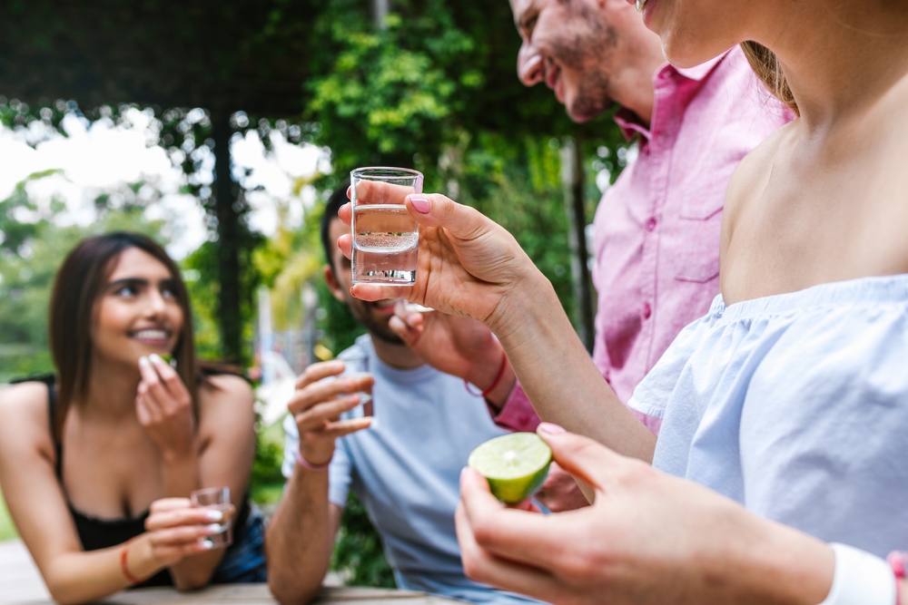 A group of friends taking shots of tequila and holding limes.