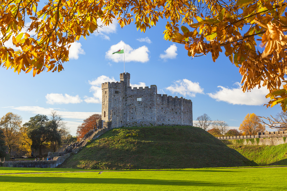 Cardiff Castle with a green lawn and leaves changing colors in the foreground.