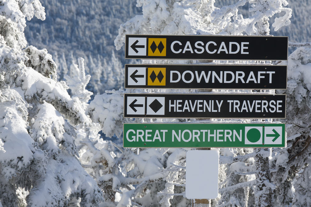 A sign on a ski mountain pointing to three difficult trails in one direction, and an easy green the opposite way.