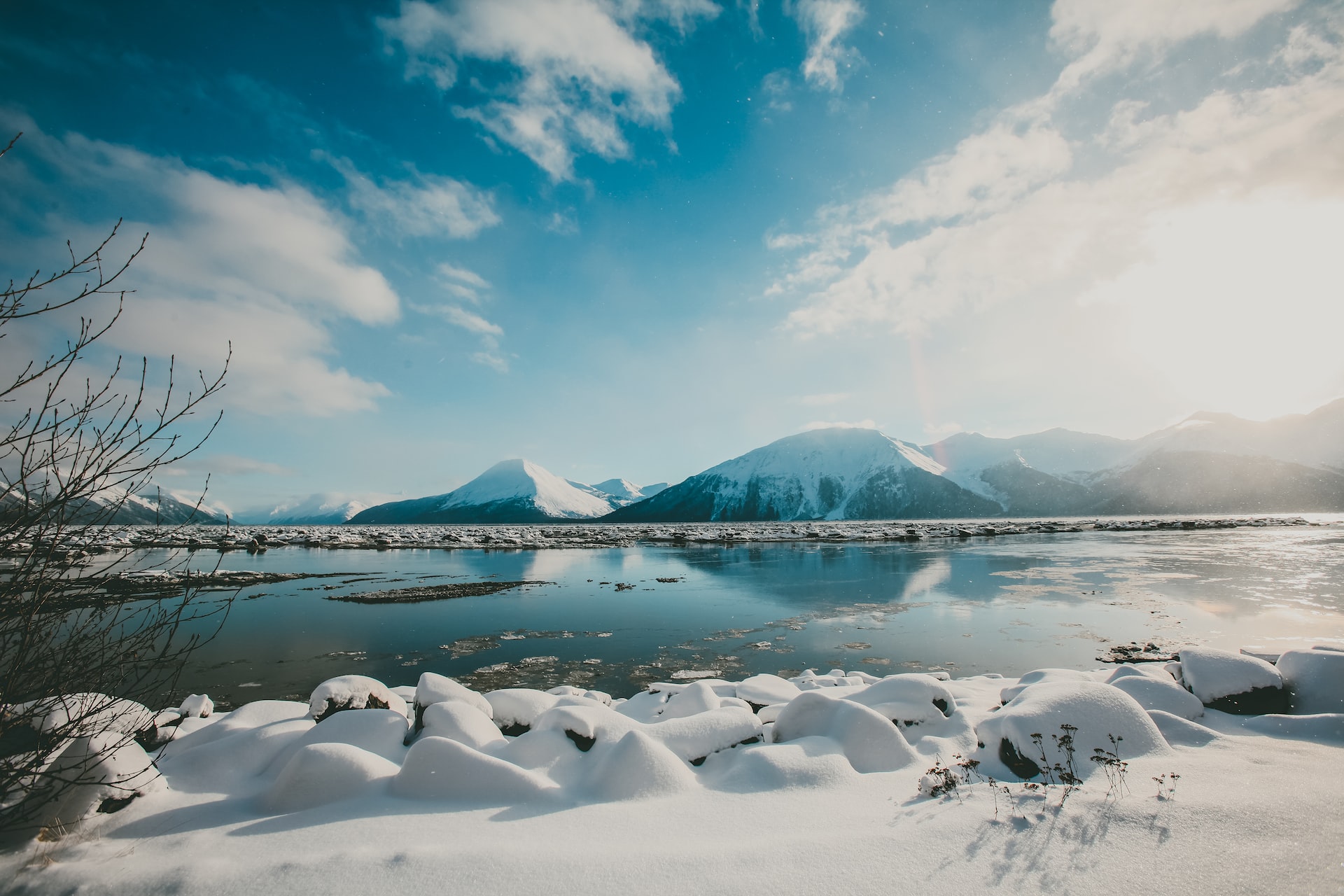 Blue skies, flat-calm lake, and large mountains covered in snow.