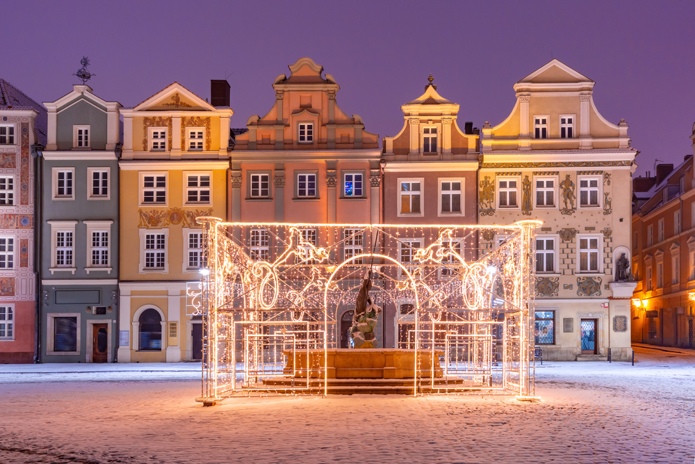A fountain in Poznan, poland covered in snow and Christmas lights.