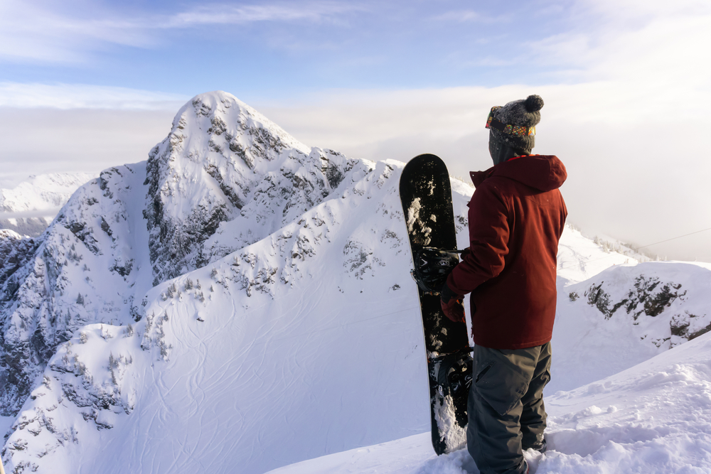 Snowboarder with his back turned looking across one of the snowy peaks at a Canadian ski resort.