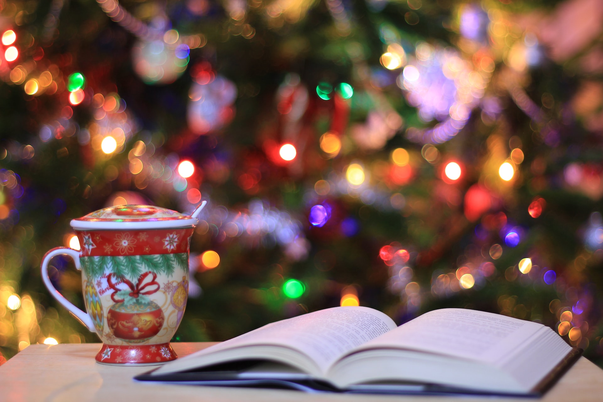 A book opened to a middle page with a coffee mug beside it in front of a Christmas tree.