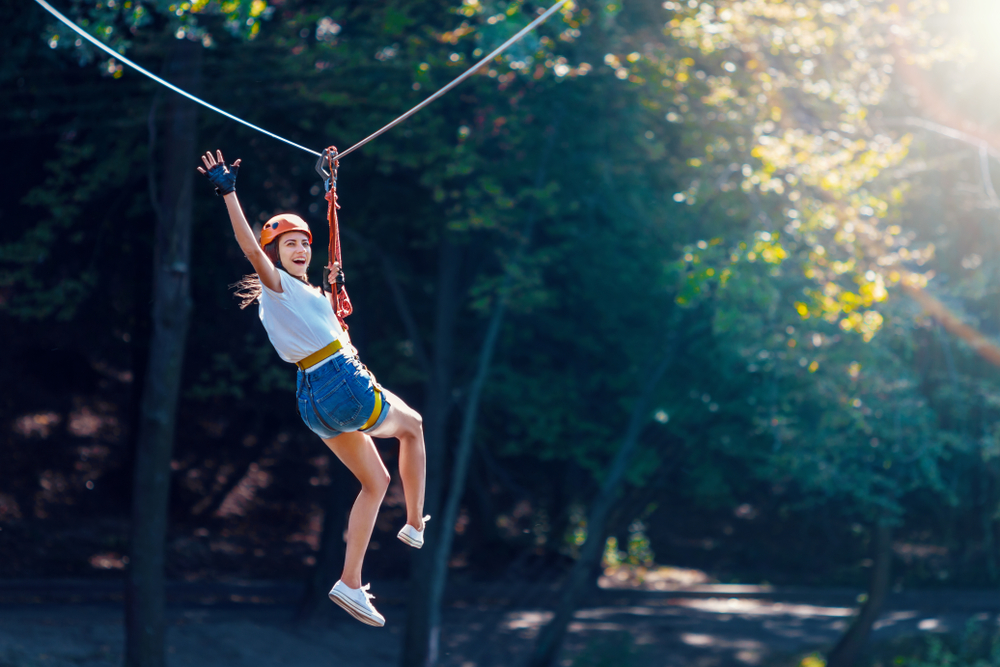 Happy woman smiling and waving while on a zipline in forest.