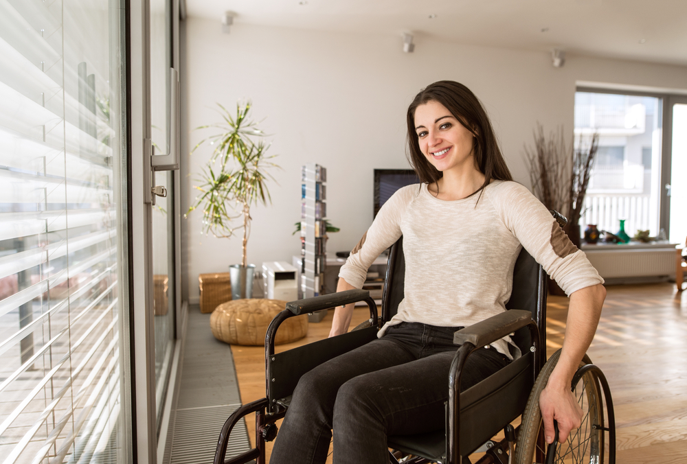 Young disabled woman in wheelchair at home in living room.