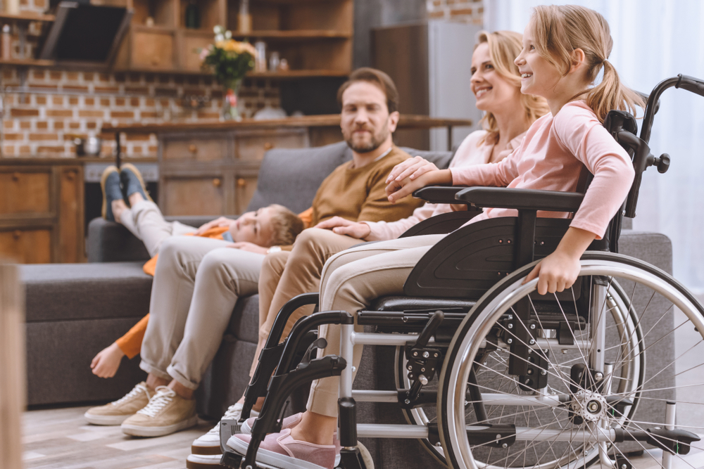 Happy family with disabled young daughter in wheelchair spending time together at home.