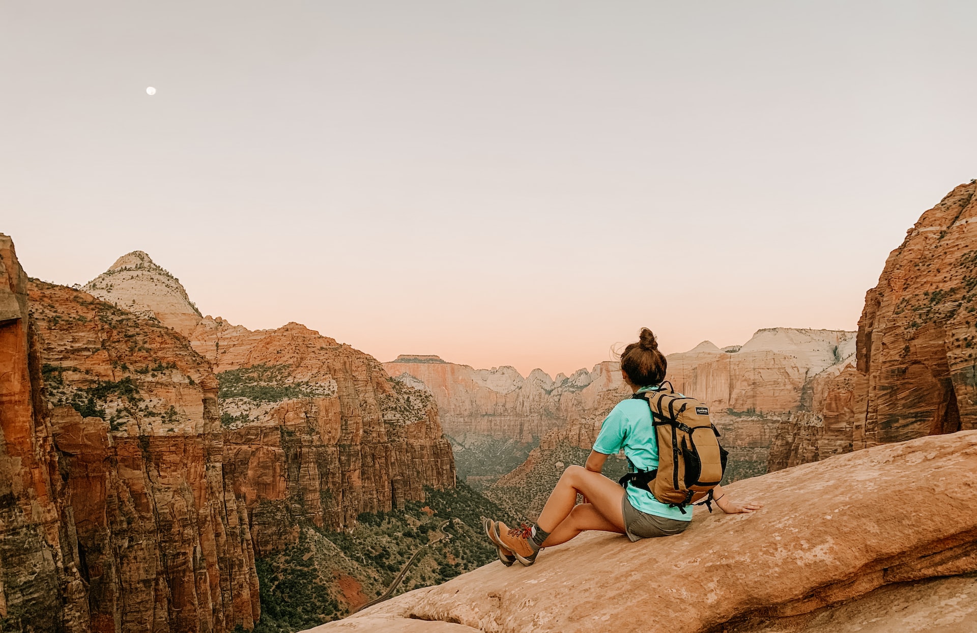 A woman wearing a backpack on a cliffside in Zion National Park.