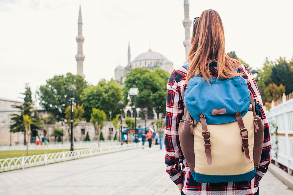 Young female traveler with a backpack looking at the Blue Mosque, a famous tourist attraction in Istanbul.