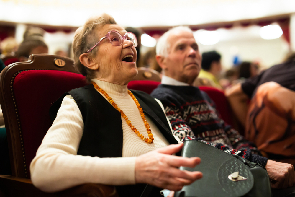 Mature spouses are interested in watching ballet performance in theater hall.