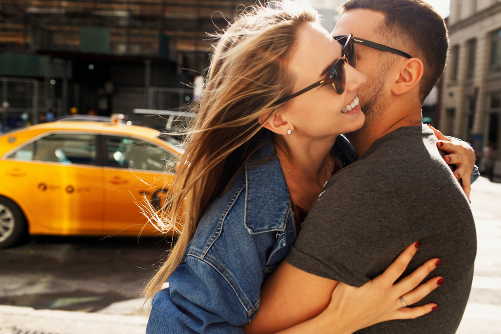 A couple emrbace in front of a New York City taxi.