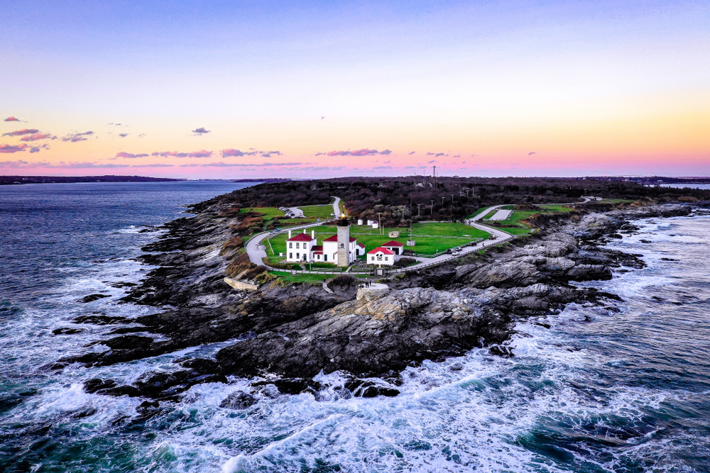 The sun setting on the rocky outcrop and manicured green lawn of Beavertail Light in Rhode Island.