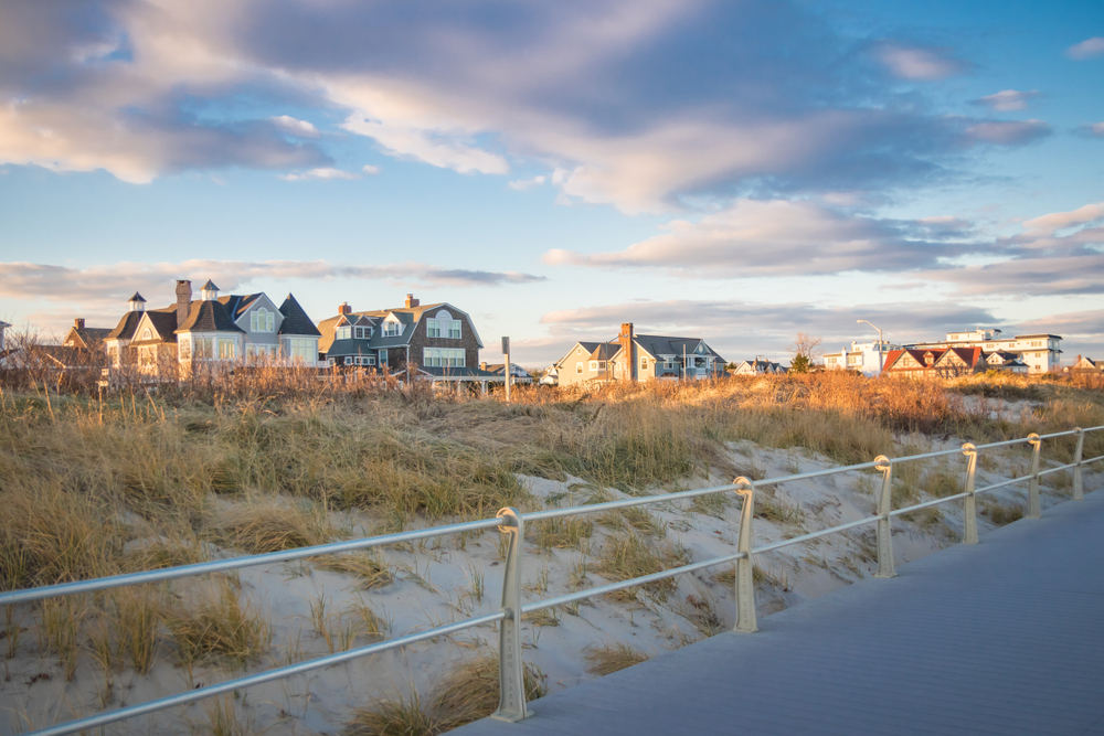 Luxury summer homes along the coastline and board walk in Spring Lake, New Jersey, against pastel-colored skies.
