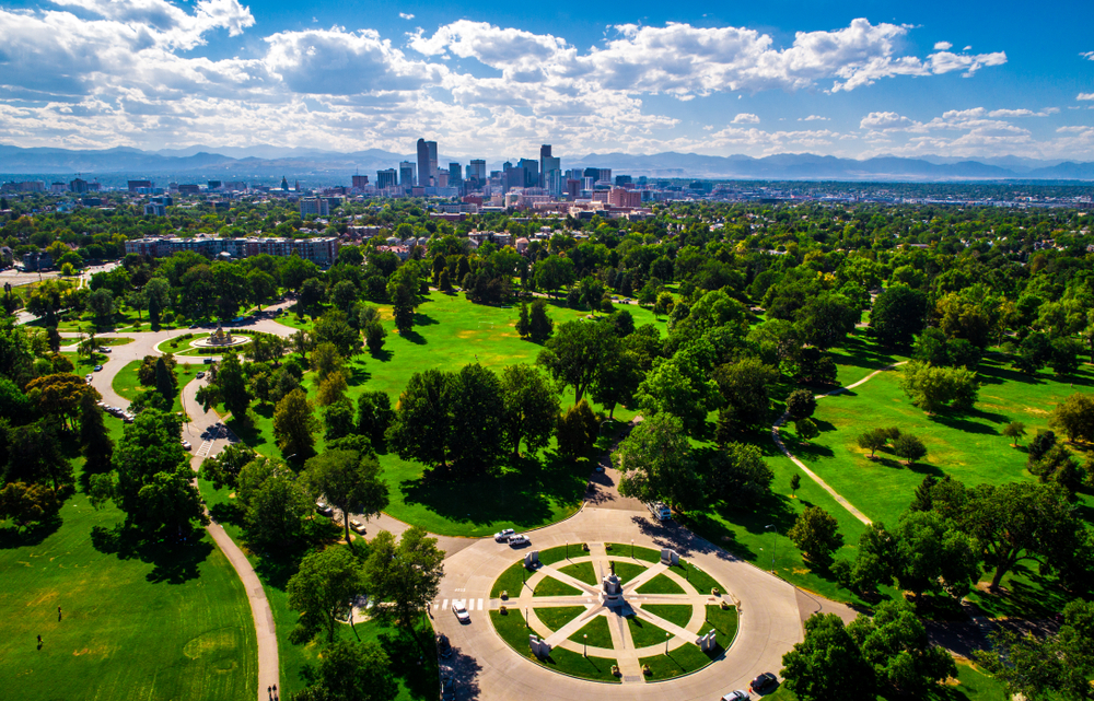 City park in the foreground on a green, summer day with the city of Denver in the background and blue skies interspersed with white clouds above.