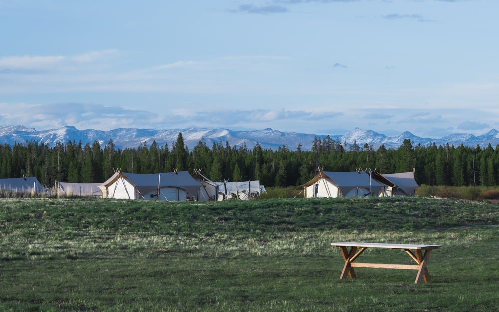 Safari-inspired glamping tents set up on a prairie with mountains behind them in the distance.