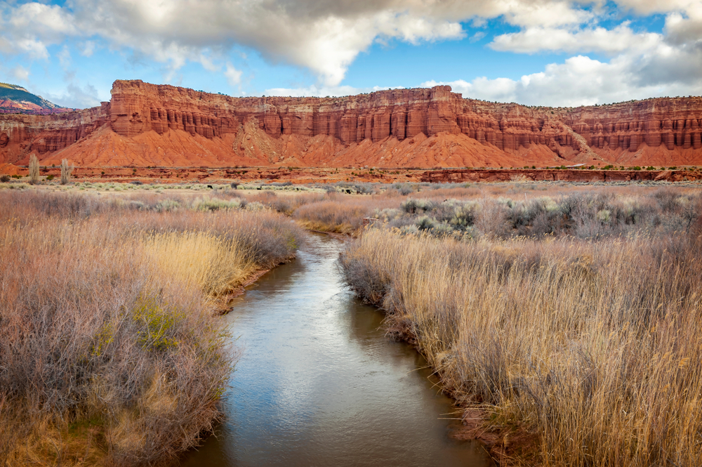 The Fremont River in the foreground flowing towards red sandstone cliffs in the distance.