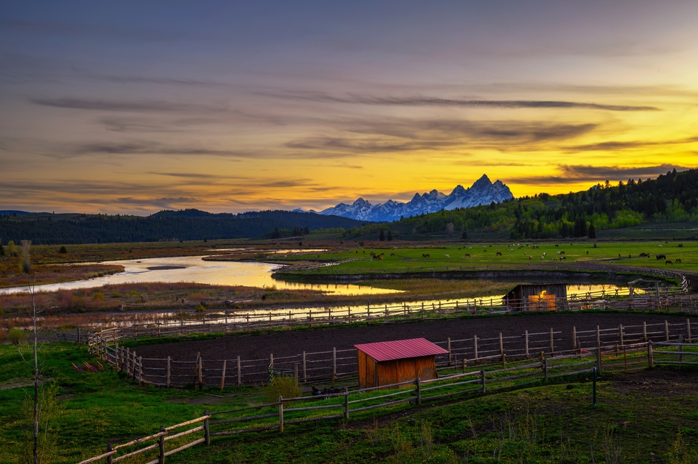 Sunset above the Grand Teton mountains with the Buffalo Fork of the Snake River and a ranch with horses in the foreground.