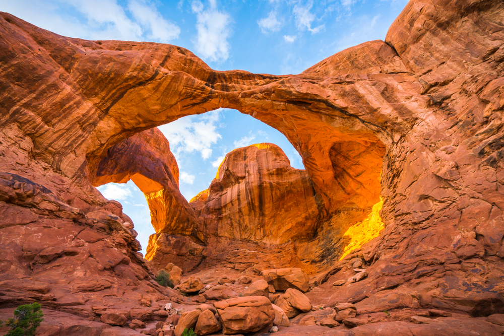 Double Arch in the afternoon with blue sky and clouds above and shadows and light on the rocks, taken in Arches National Park in Utah.