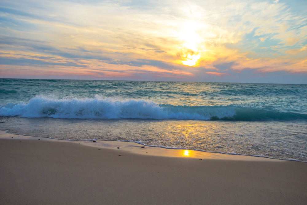 The beach during sunset as waves crash onto the sandy coast of Lake Michigan.