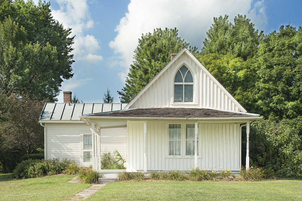 The famous American Gothic House, a small farm house with a green front lawn and trees behind it.