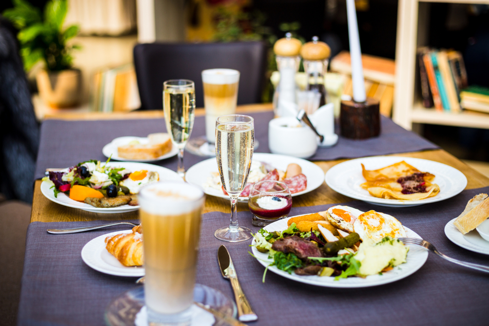 Brunch including a glass of champagne with appealing food on a multiple plates.