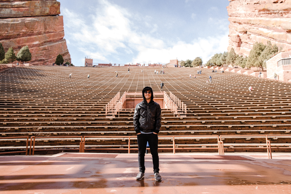 Man stands wearing hoodie in front of Red Rocks Amphitheater.