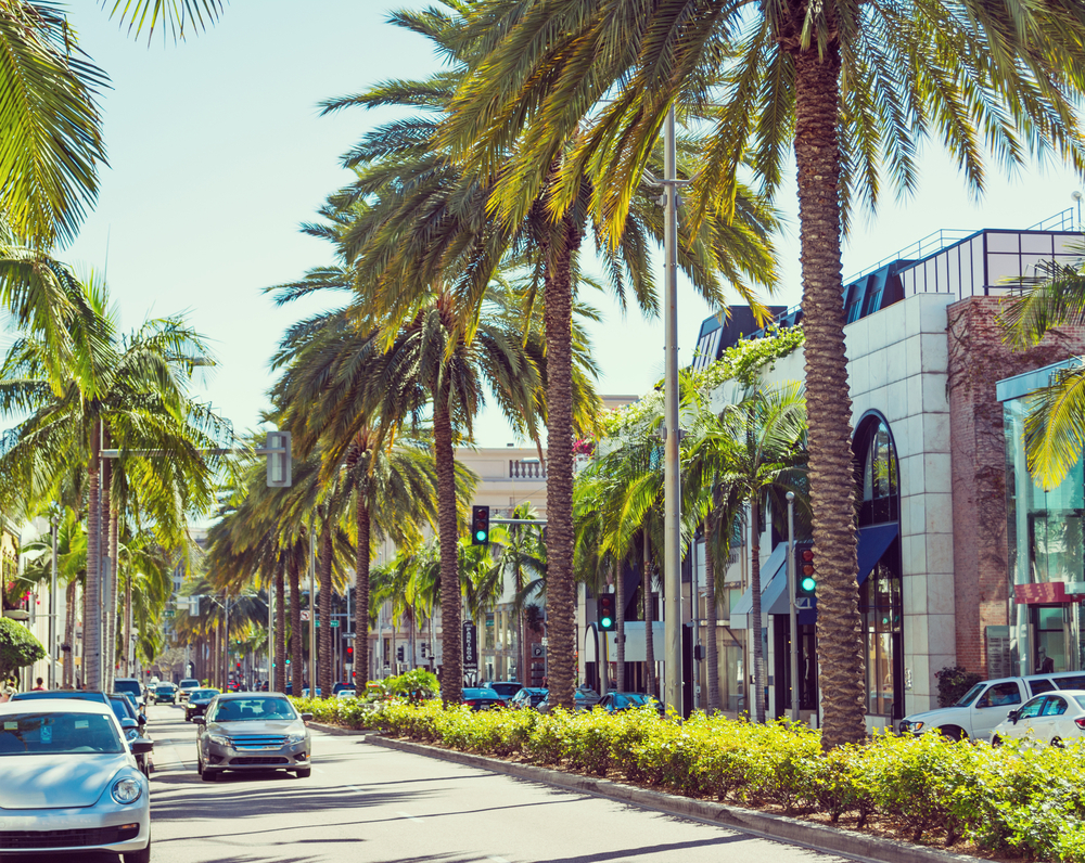 High-end cars and palms lining Rodeo Drive on a sunny day in Los Angeles, California.