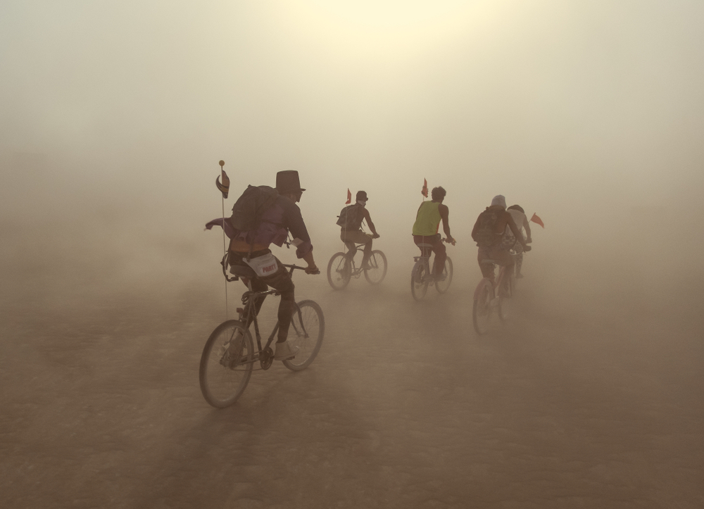 Group of people riding bikes in dust storm in the desert.