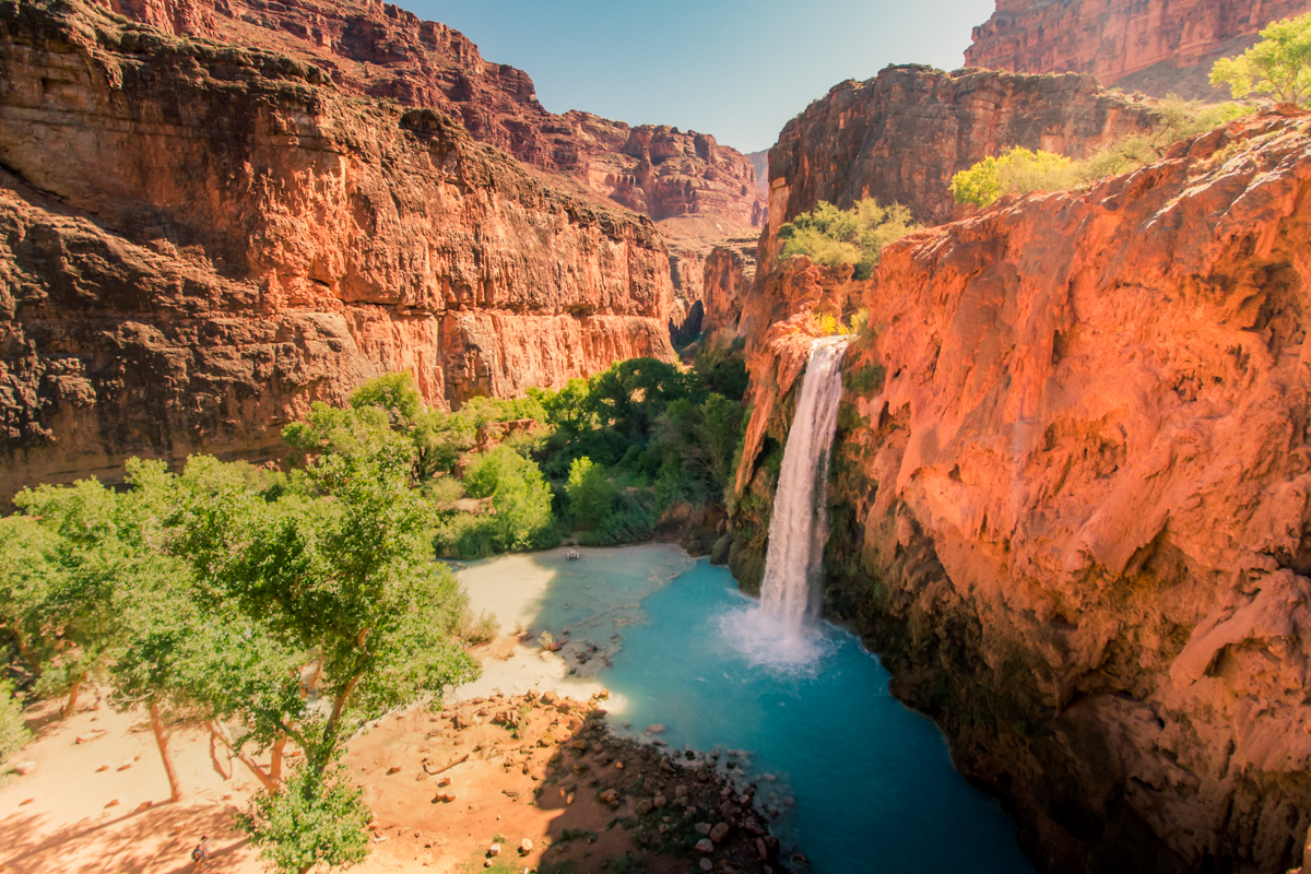 A waterfall spilling aquamarine water over burnt orange cliffs in Havasupai Falls, Arizona.