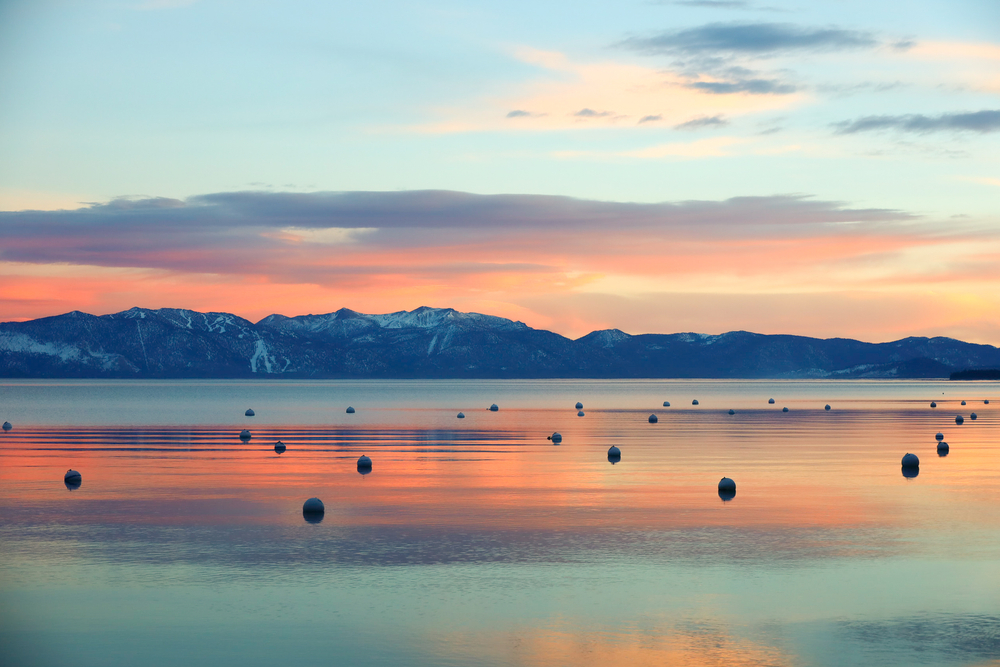 A sunset over Lake Tahoe with mountain reflections and bright, sherbert-like colors.