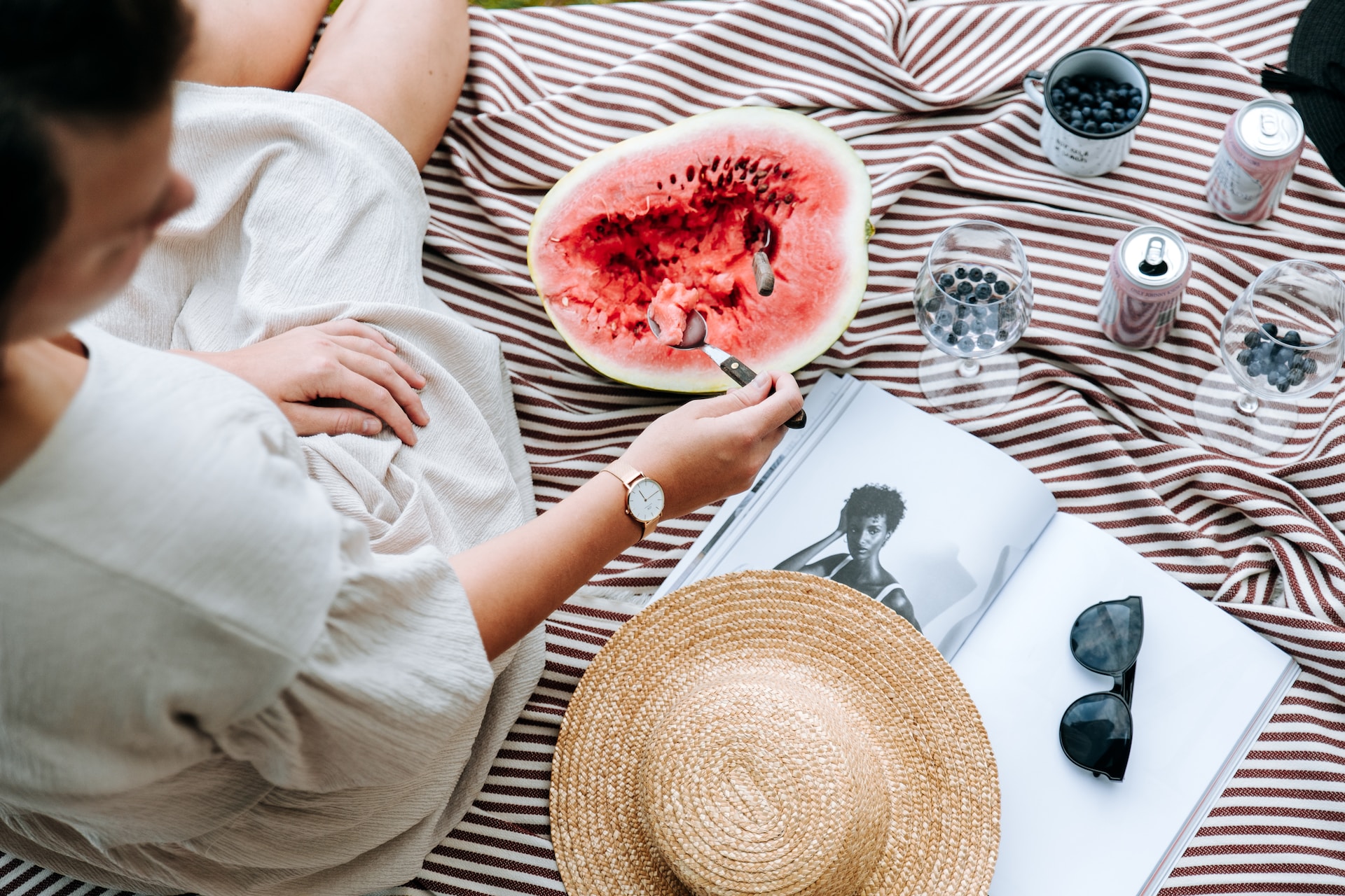 Woman eating watermelon on a blanket.