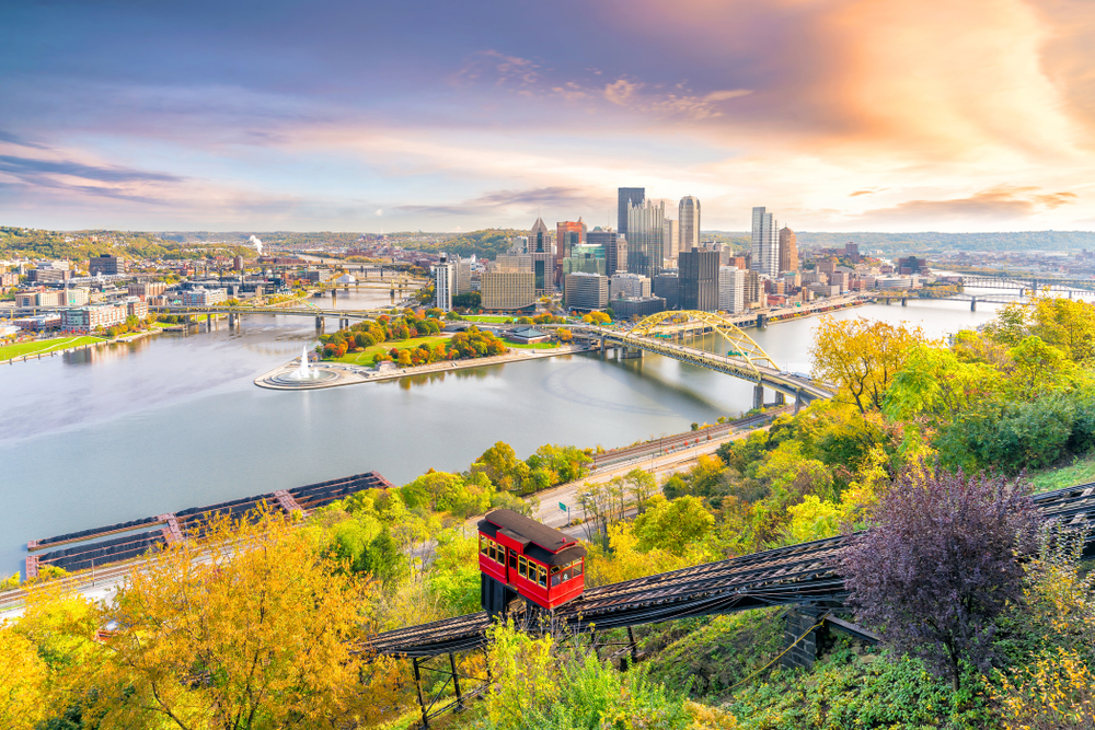 A sunny scene of downtown Pittsburgh and a red trolley car going up the side of a hill.