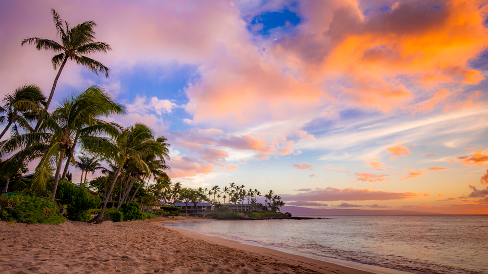 Napili Bay sunset in West Maui, beach, sand, and palm trees visible.