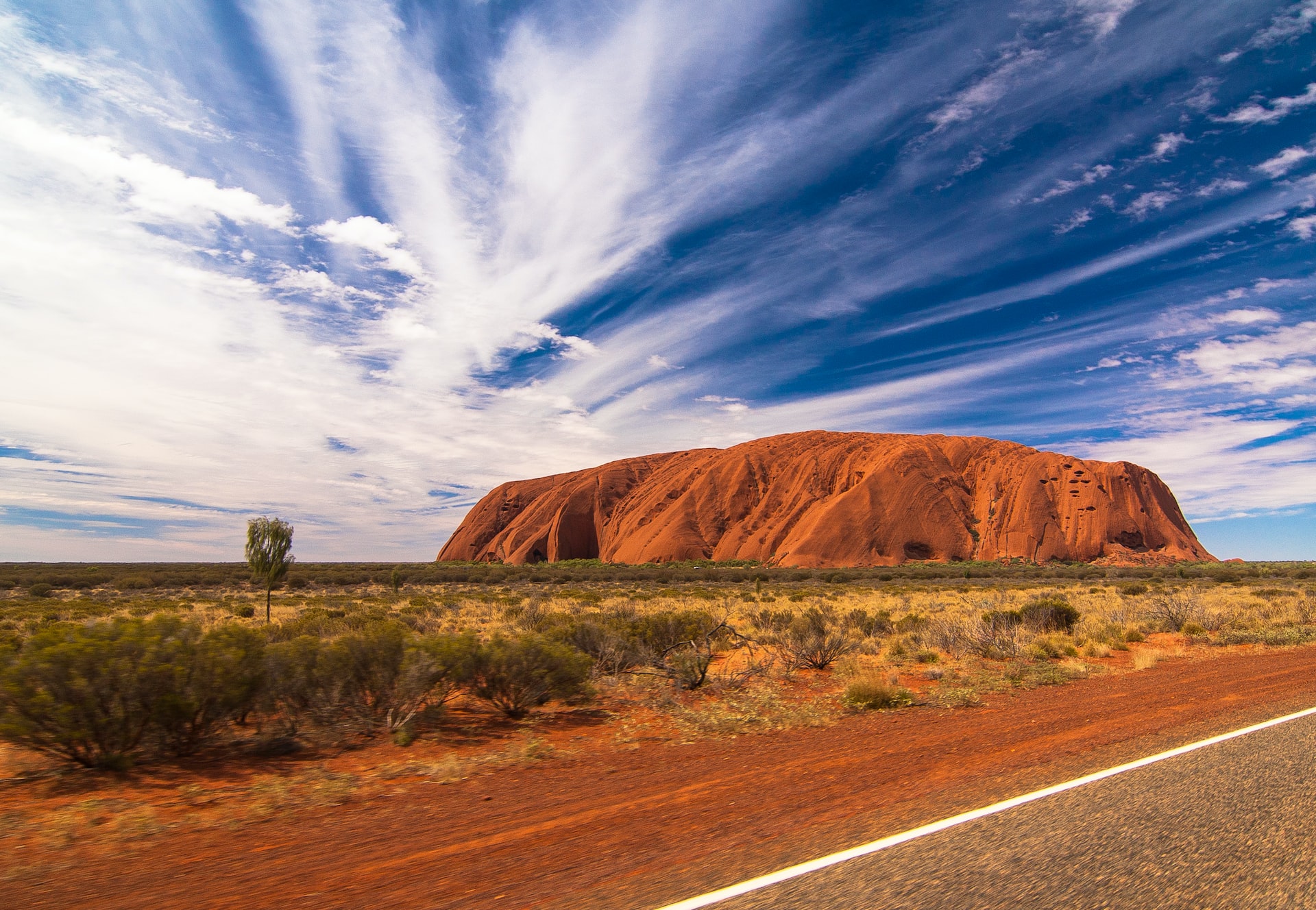 The red sand of Uluru under a blue sky with some clouds in Australia.