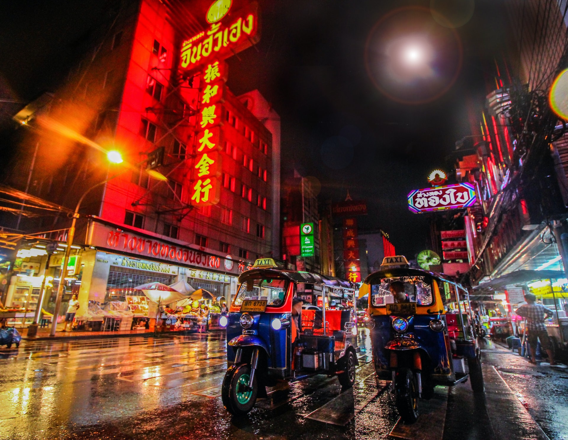 View of two tuk-tuks in Bangkok’s neon-lit Chinatown at night.