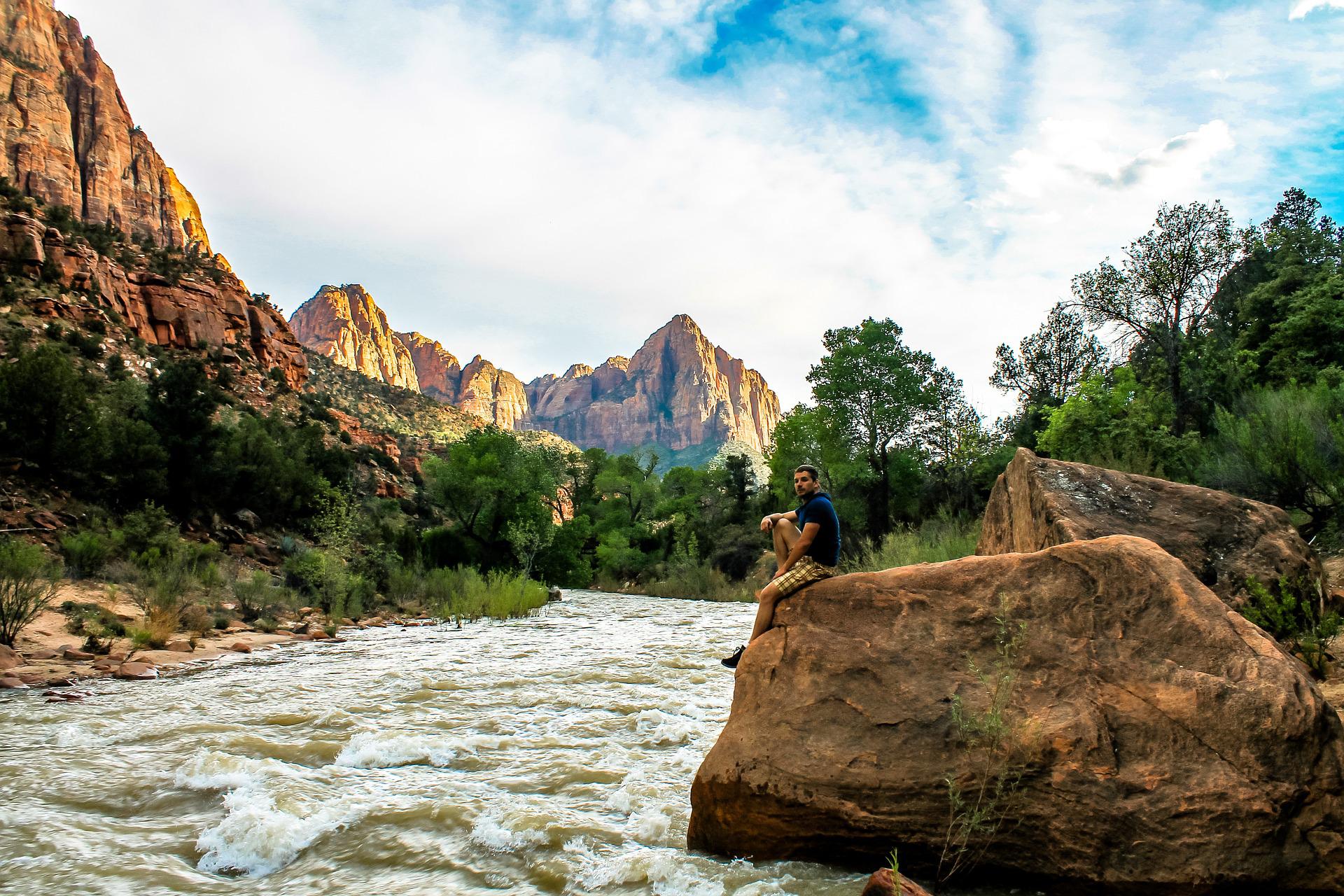 A man sits on a boulder next to a fast-moving river in Zion National Park.