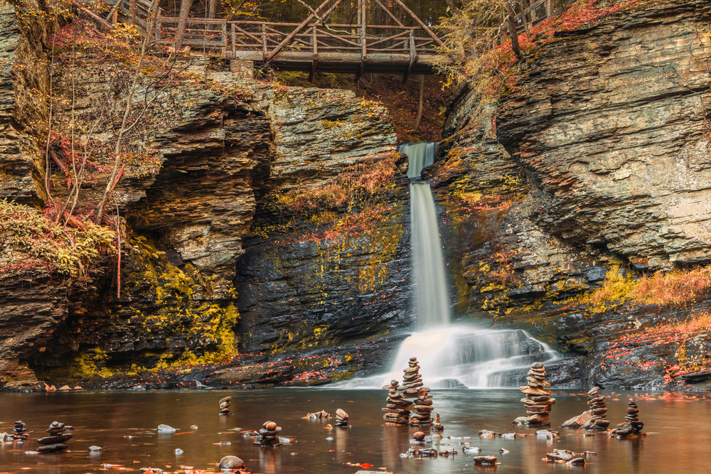 A footbridge and cairns surround Deer Leap Falls in peak fall foliage at the Delaware Water Gap in Pocono Mountains, PA.