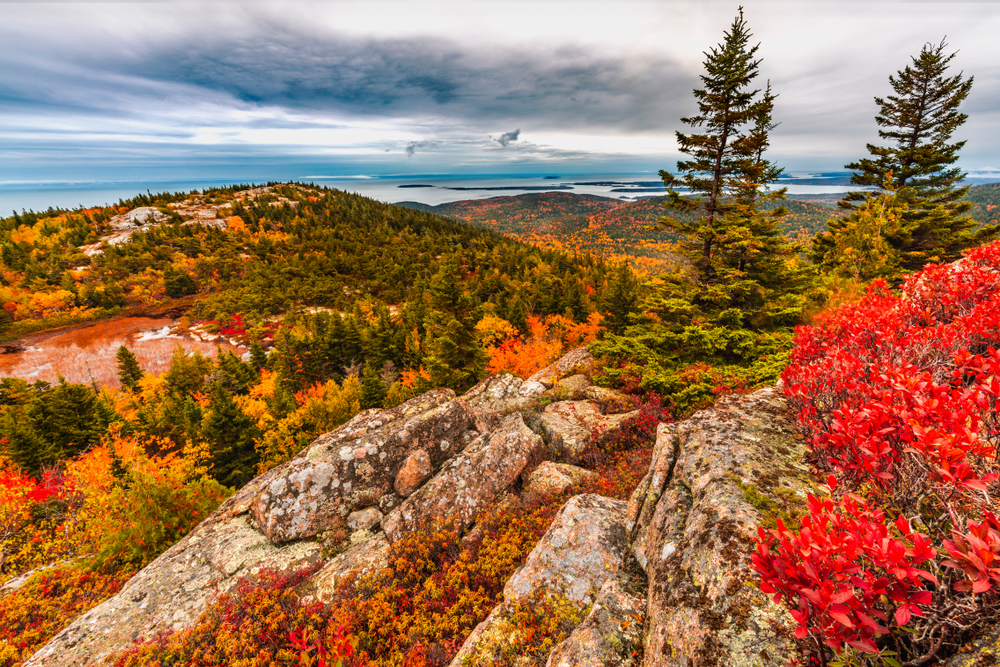 Fall colors in Acadia National Park Island in Maine high on mountain ledge overlooking Atlantic Ocean with fog and lake in background.