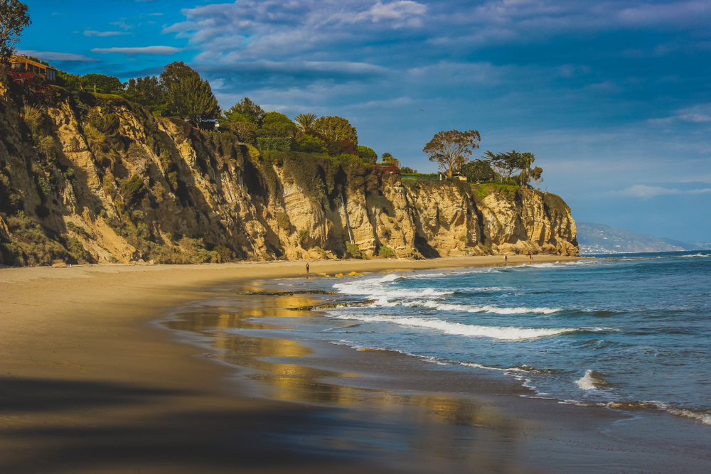 Beachside view of beautiful blue Pacific Ocean and stunning cliffs surrounding Dume Cove on a sunny day with clouds in the sky, Point Dume, Malibu.