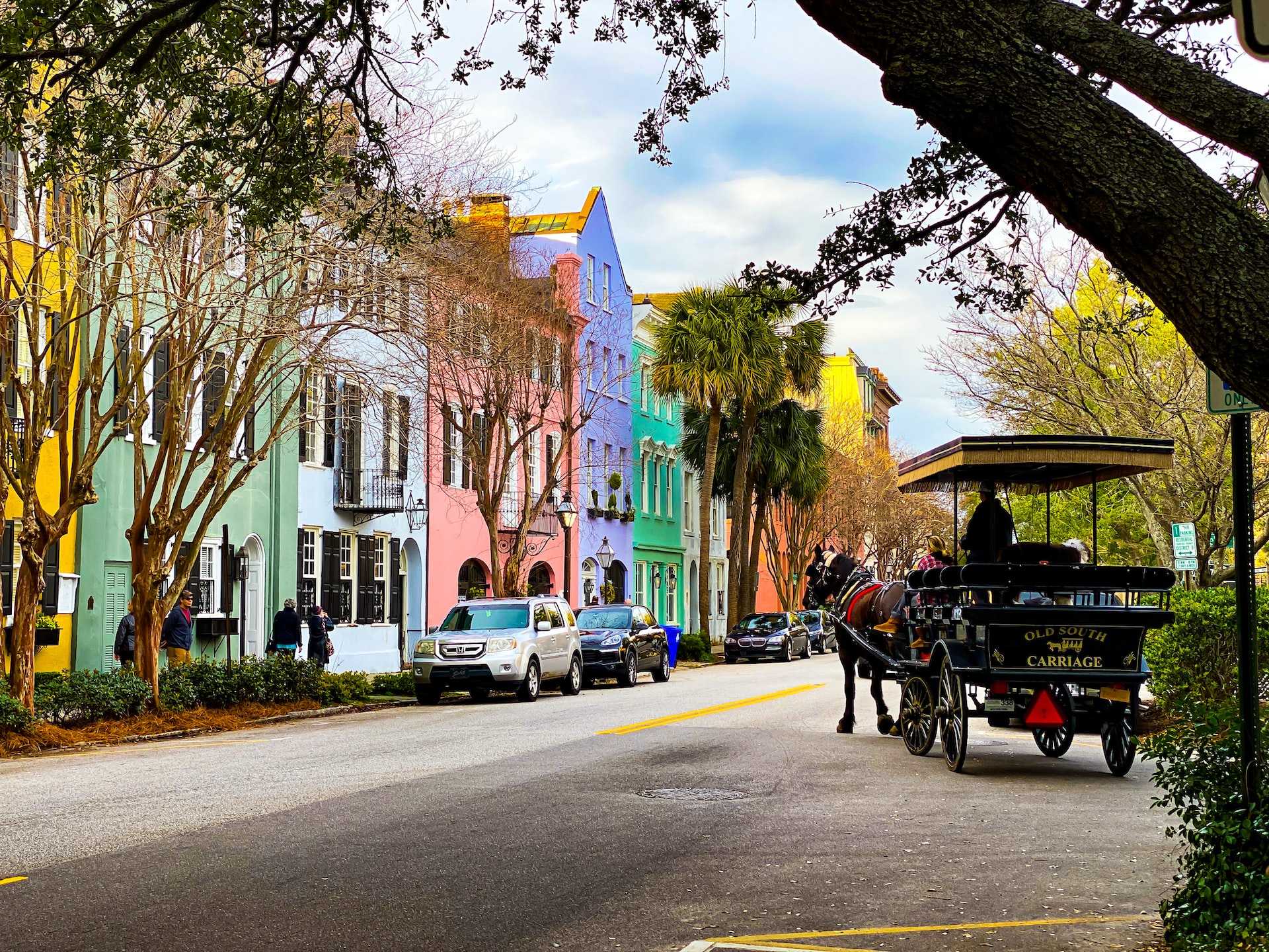 People riding on a horsedrawn cart in Charleston next to colorful buildings.