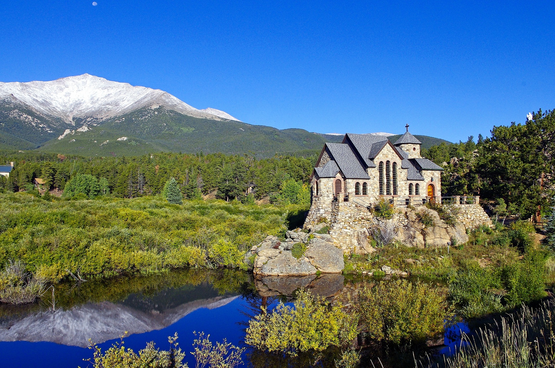 The Chapel on the Rock is a functioning Catholic chapel and tourist landmark in Allenspark, Colorado, pictured here with a white-capped mountain in the distance.