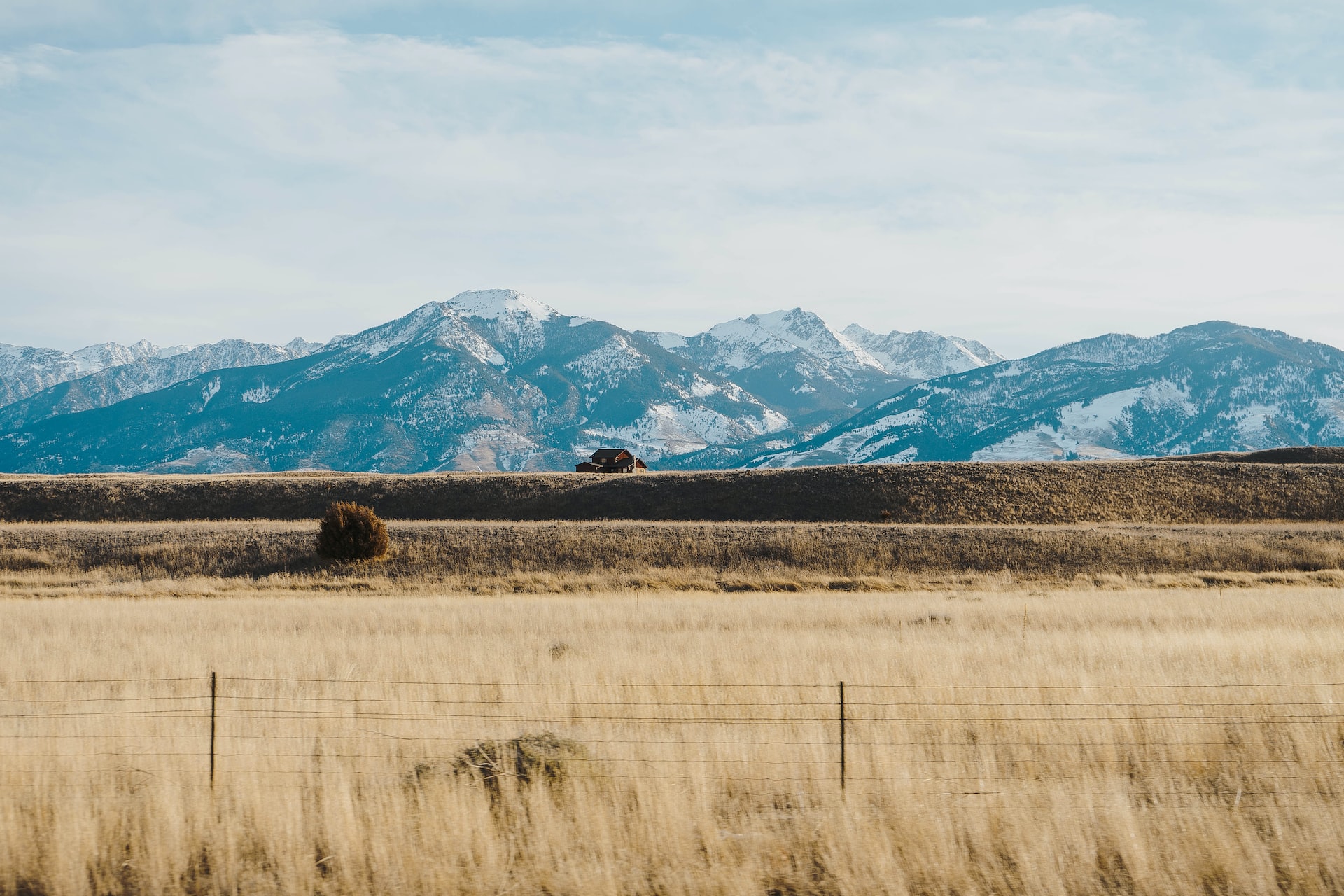 Golden fields with massive mountain ranges in background and a house perched on a ridge.