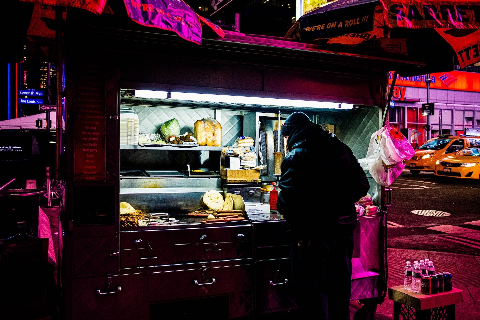 A man standing preparing in food in front of a Halal meat cart in NYC at night.