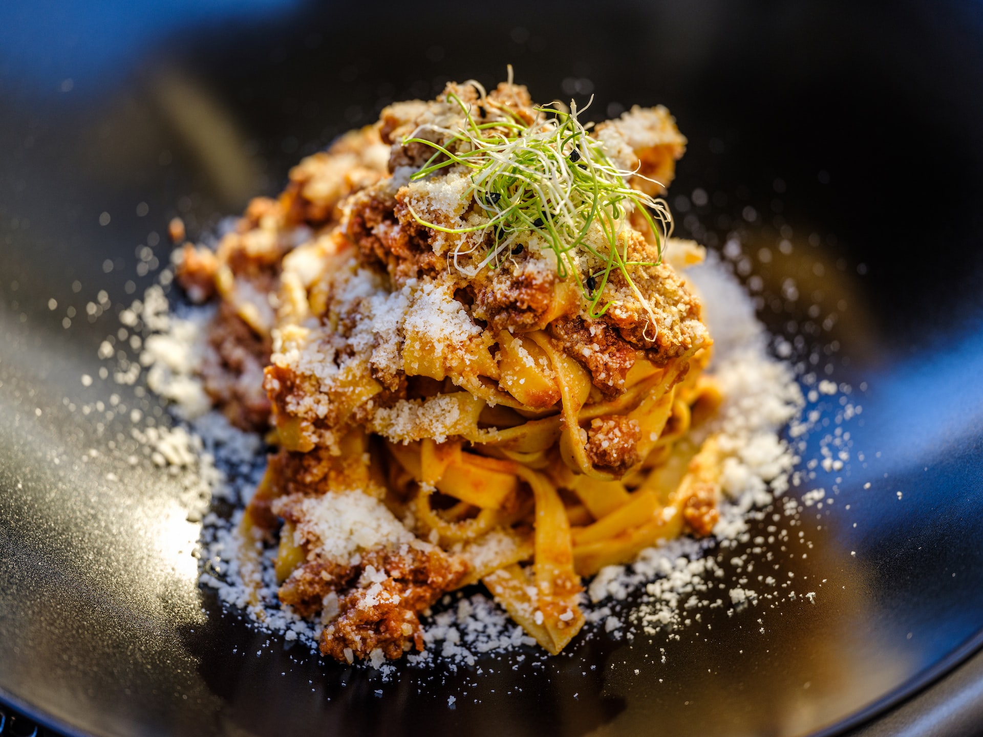 Upscale Italian food; pasta piled high on a black plate with grated cheese.
