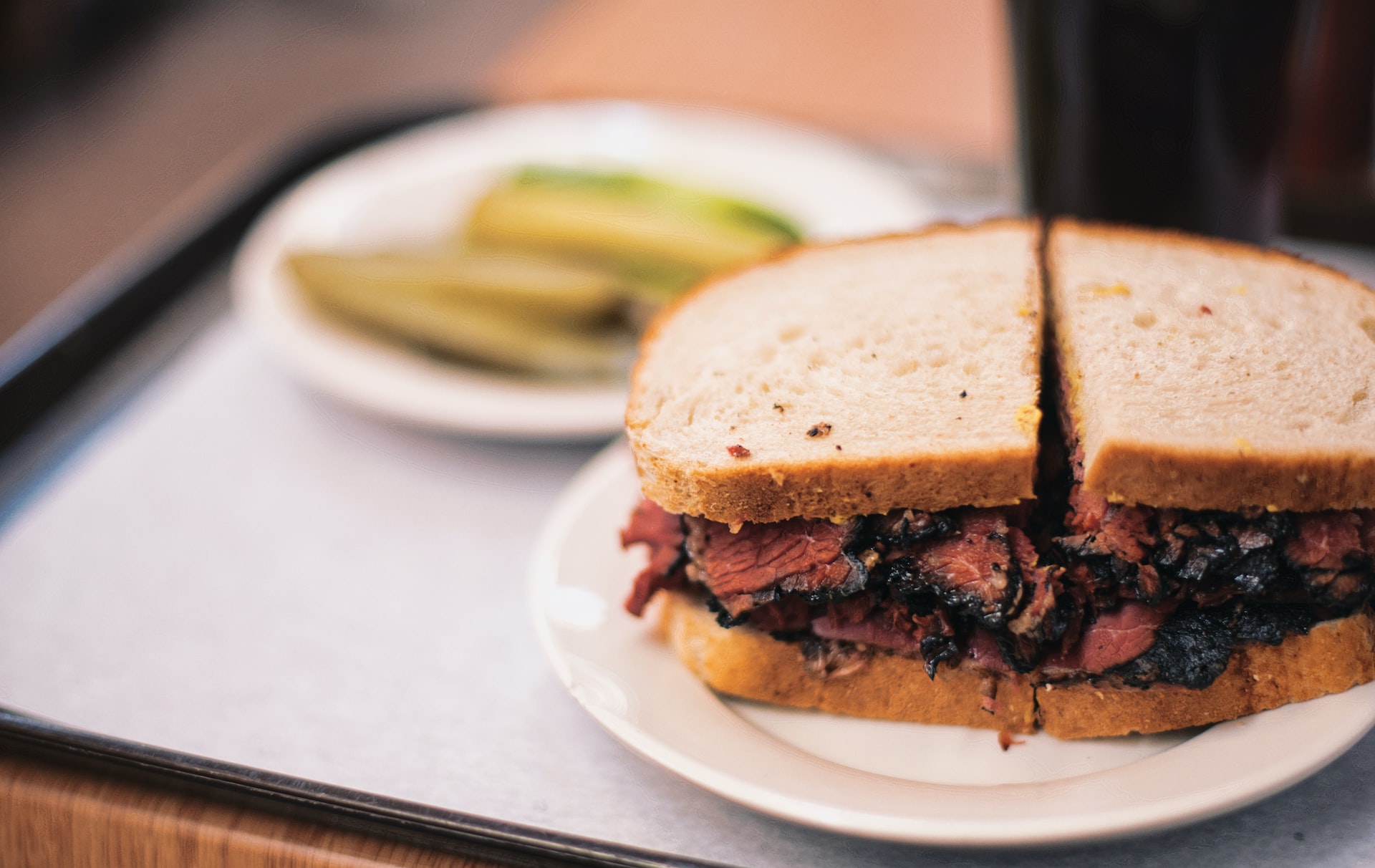 A pastrami sandwich with a side of pickles.