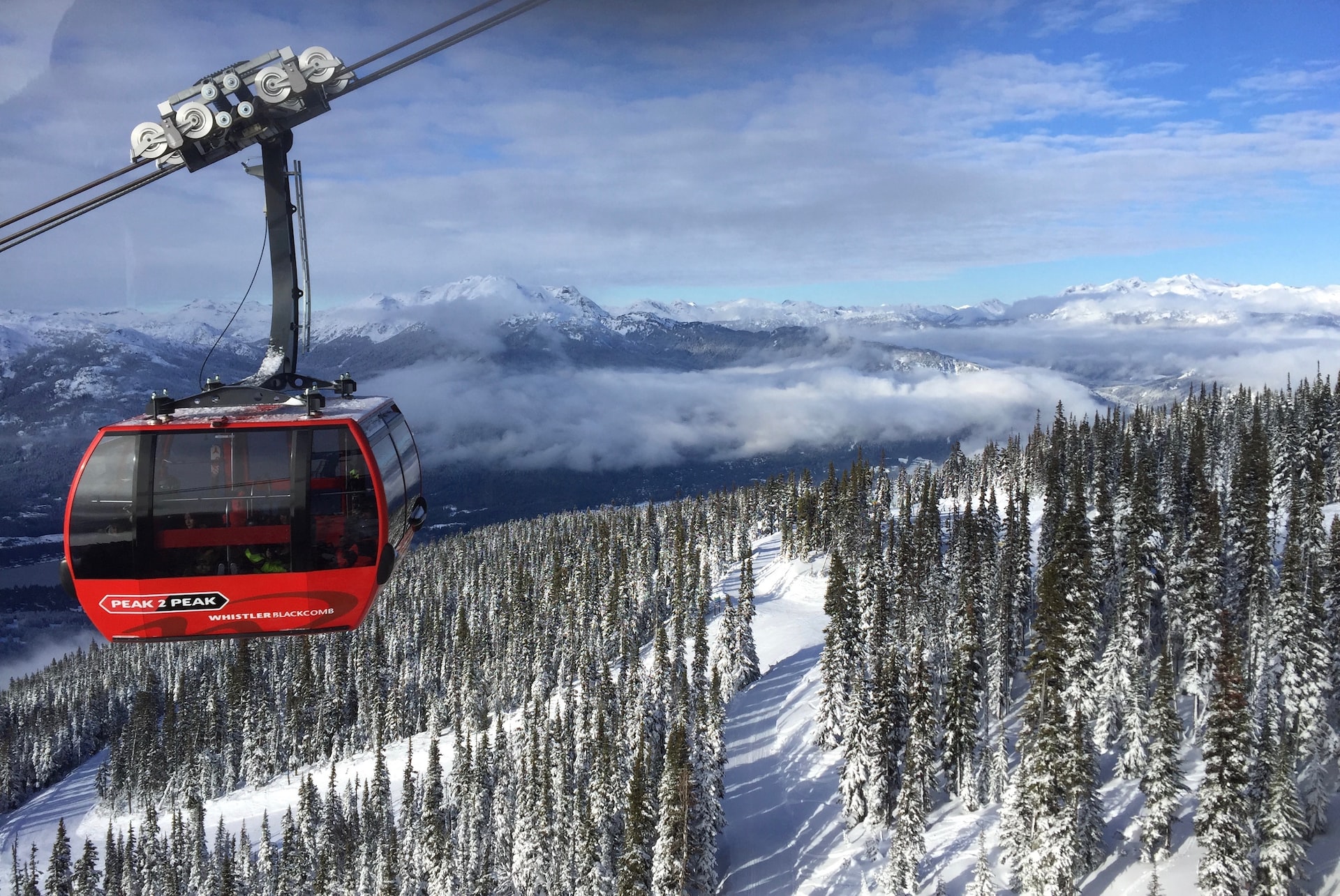 A red cable car running above a wintery mountain.
