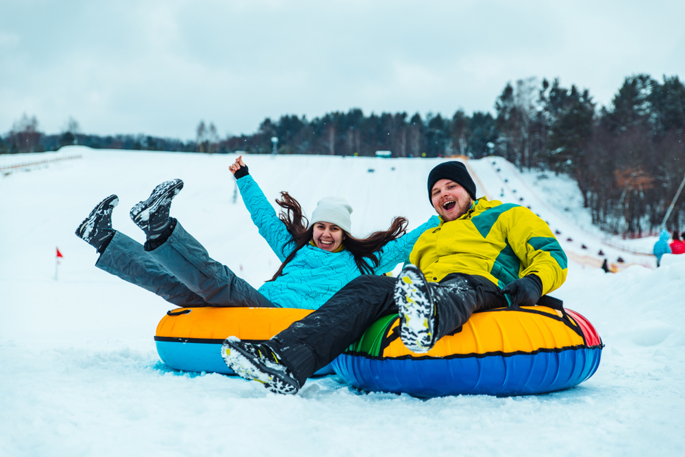 Couple having fun sliding down on a couple of snow tubes.
