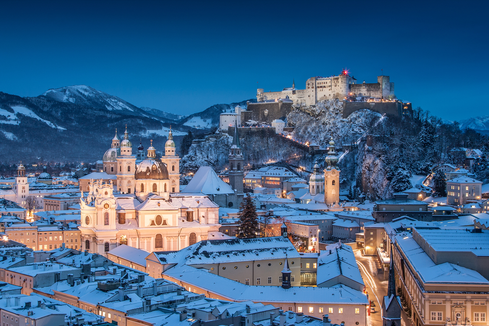 Classic view of the historic city of Salzburg with Salzburg Cathedral and famous Festung Hohensalzburg illuminated in beautiful twilight during Christmas time in winter.