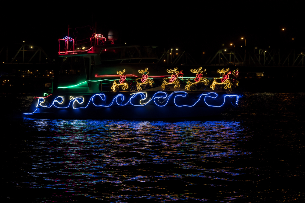 Boat adorned with Christmas lights, Santa Claus's sleigh and reindeer reflected in the water.